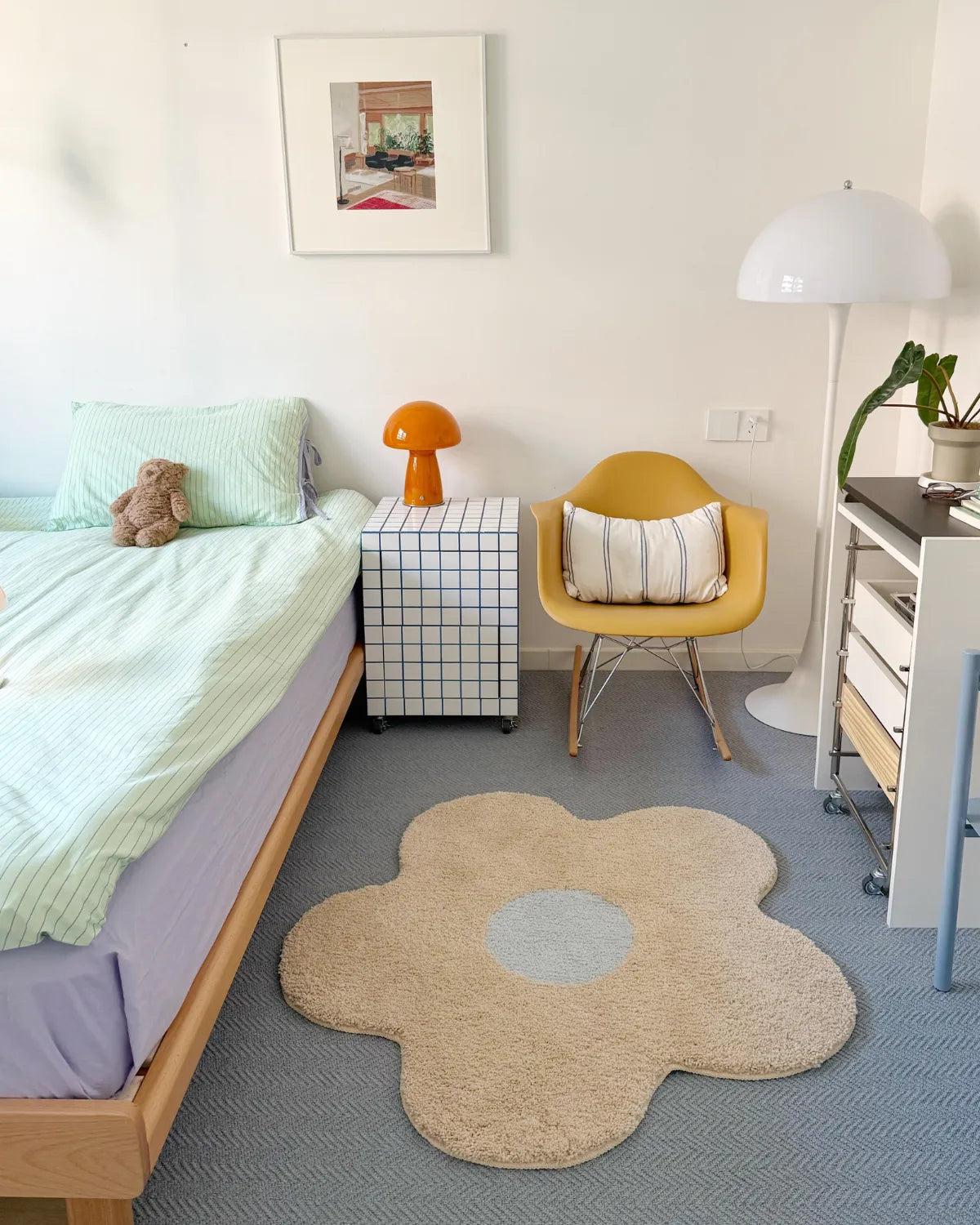 Housenfriends Maisie cream and pale blue daisy-shaped tufted rug beside a bed in a pastel bedroom.