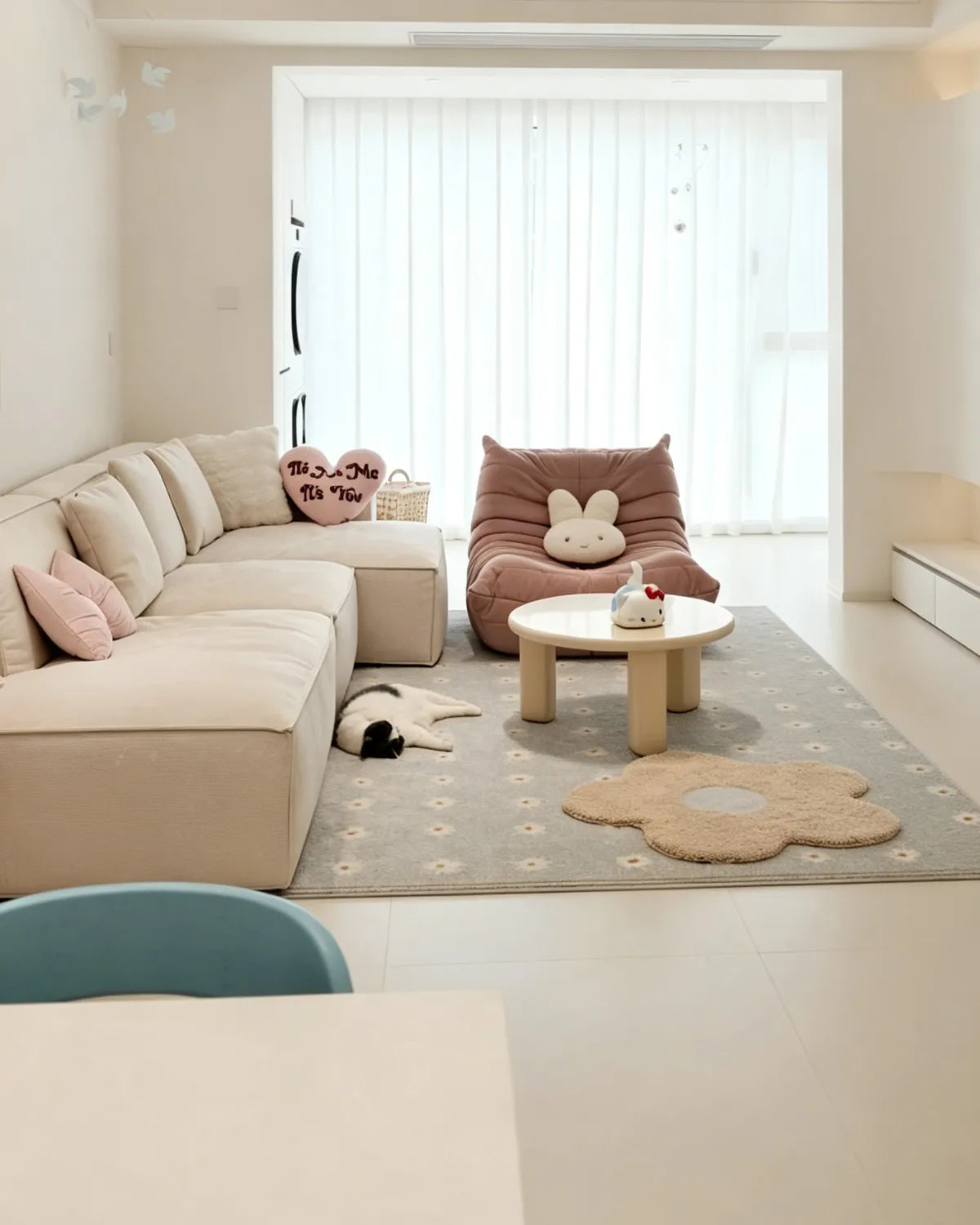 Housenfriends Maisie cream and pale blue daisy-shaped tufted rug beside a sofa in a pastel living room, with a cat nearby.