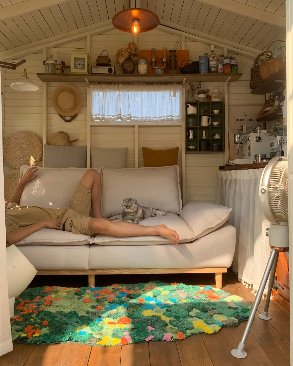 Housenfriends Merryn Green Moss Garden rug in front of a sofa in a rustic cabin living room, with a person and cat on the sofa, 80 × 180 cm.
