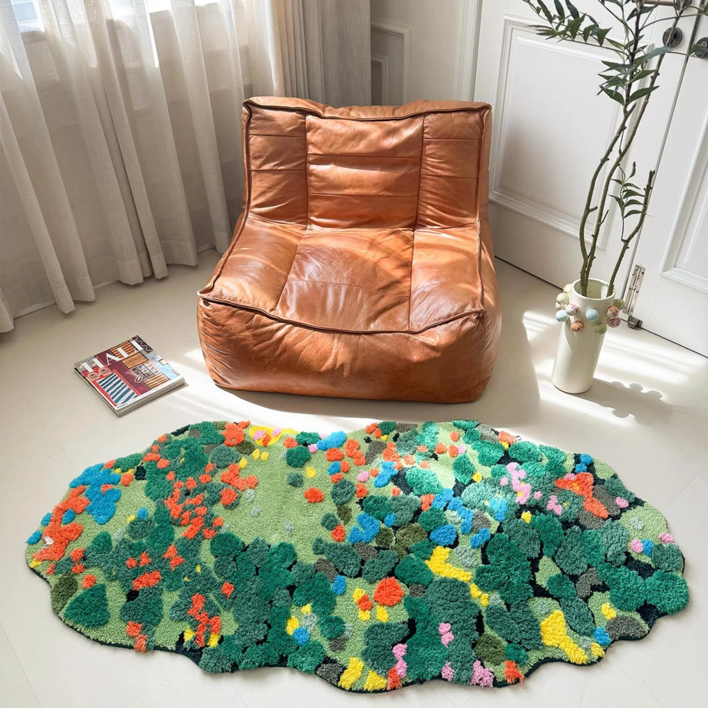 Housenfriends Merryn green moss garden irregular rug in front of a brown leather lounge chair, showing its organic outline and colourful moss-inspired pattern in a bright room.