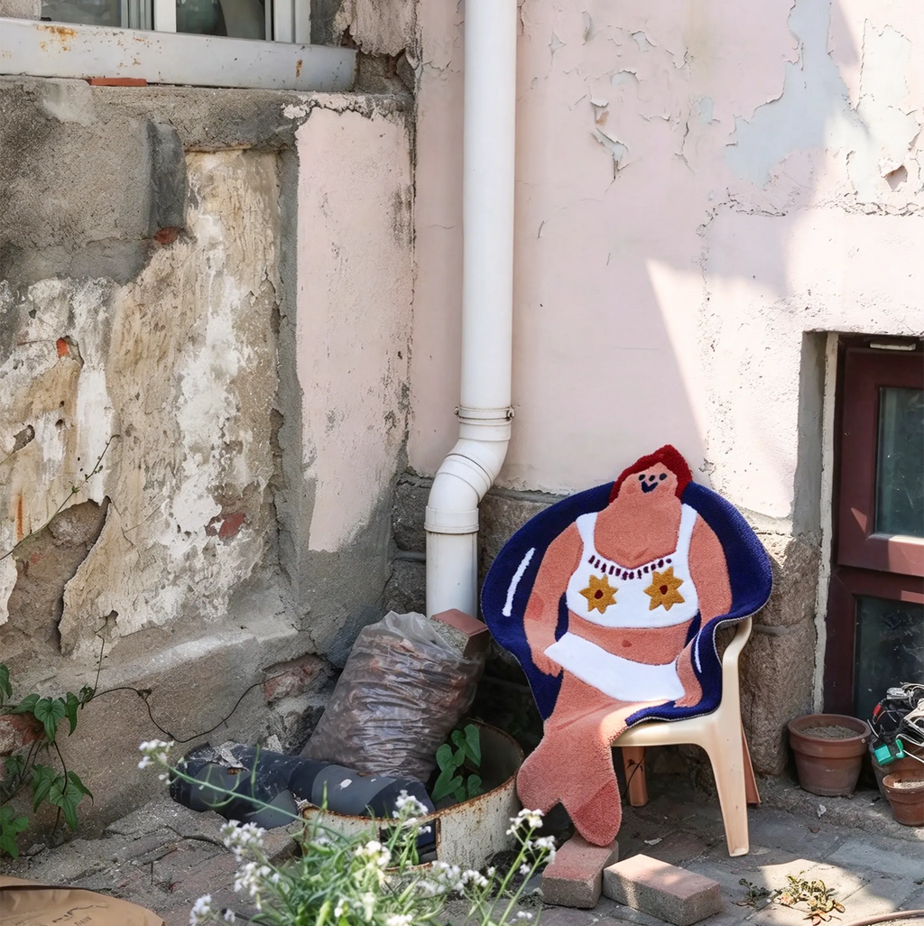 Housenfriends June swimming girl rug displayed on a small chair against a weathered wall, showing its playful illustrated silhouette.