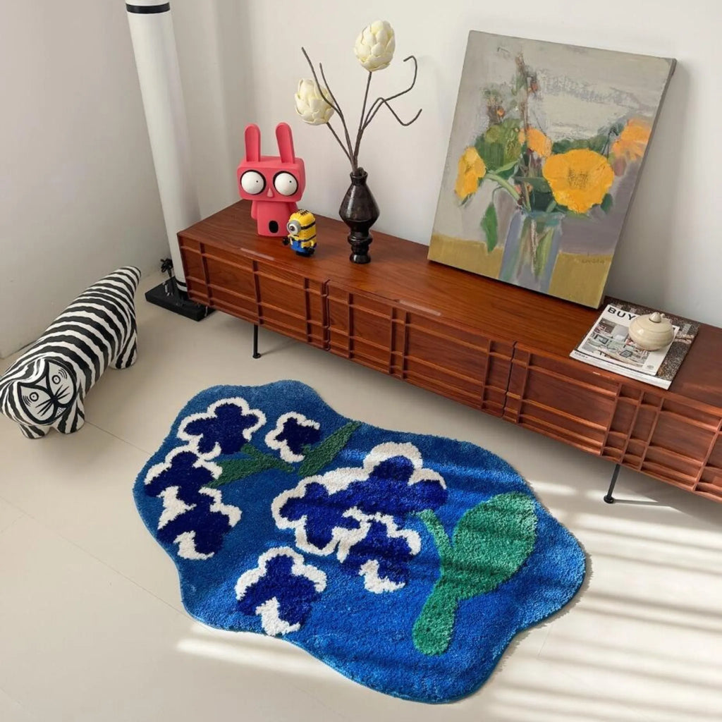 Orla blue and green floral shaped tufted rug beside a wooden sideboard in an eclectic living room with vintage-inspired decor and colourful floral artwork.